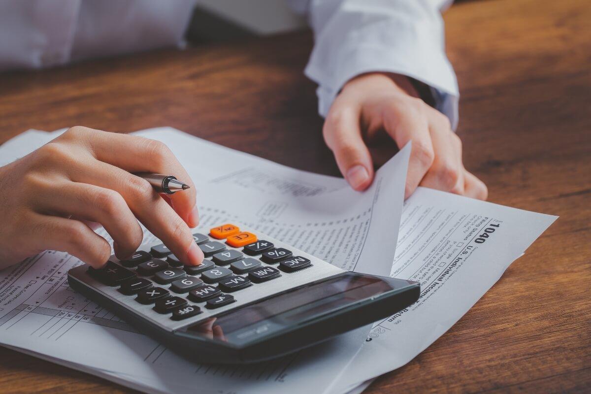 Person calculating property investment finances with calculator and documentation on wooden desk.