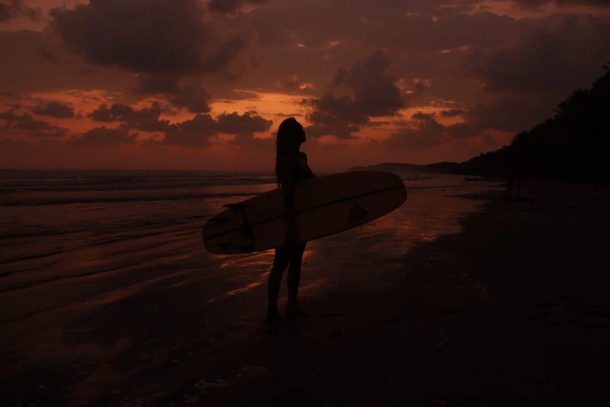 Surfer silhouette holding surfboard on a Costa Rica beach at sunset