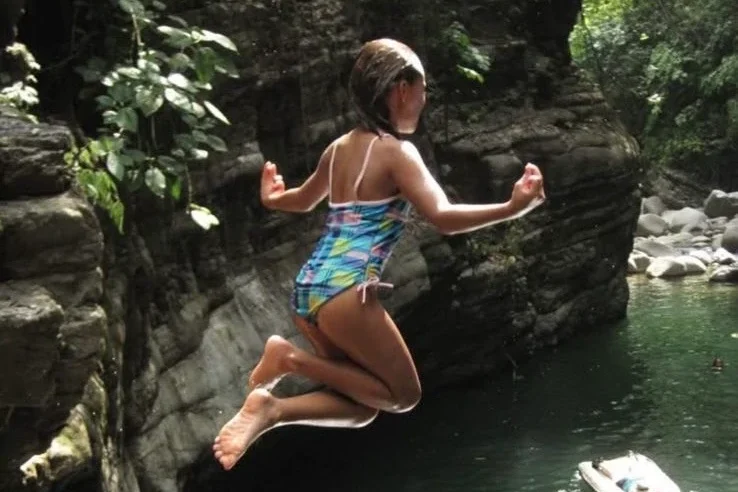 Child jumping into a river in Costa Rica surrounded by jungle and rocks